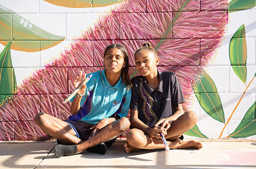 Two young girls sitting in front of a mural